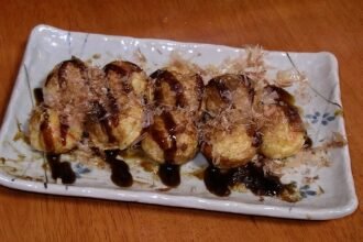 Takoyaki di atas pinggan dengan sos dan kepingan bonito