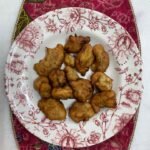 Cekodok pisang berwarna perang di atas pinggan bercorak bunga.