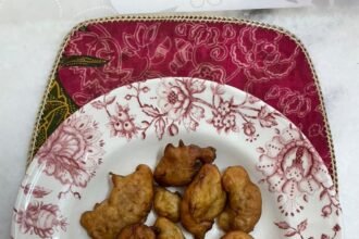 Cekodok pisang berwarna perang di atas pinggan bercorak bunga.