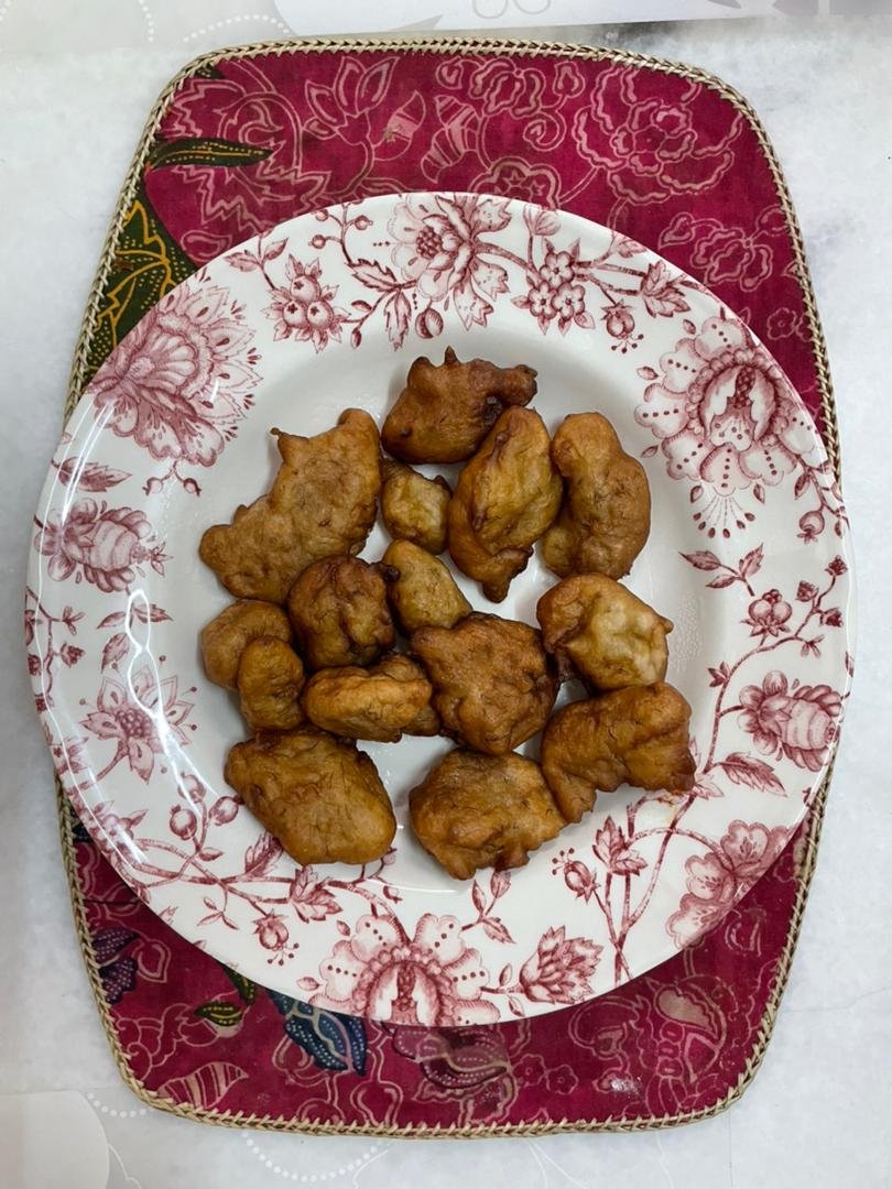 Cekodok pisang berwarna perang di atas pinggan bercorak bunga.