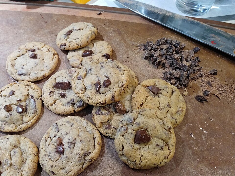 Biskut chocolate chip dan coklat cincang di atas papan pemotong