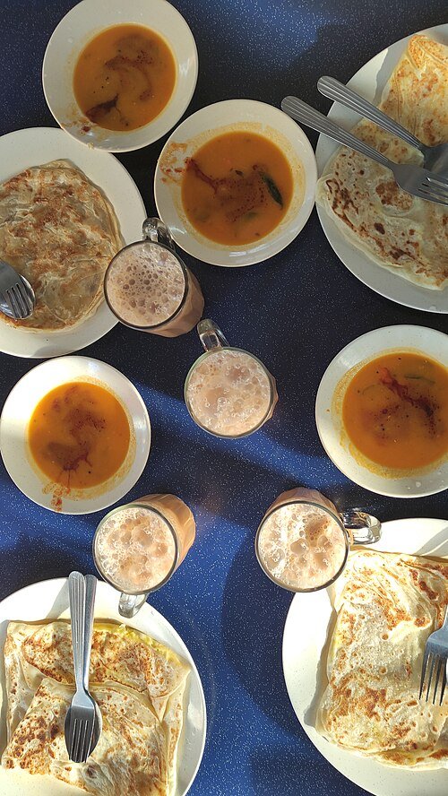 Roti canai bersama kari dan teh tarik di sebuah kedai Malaysia