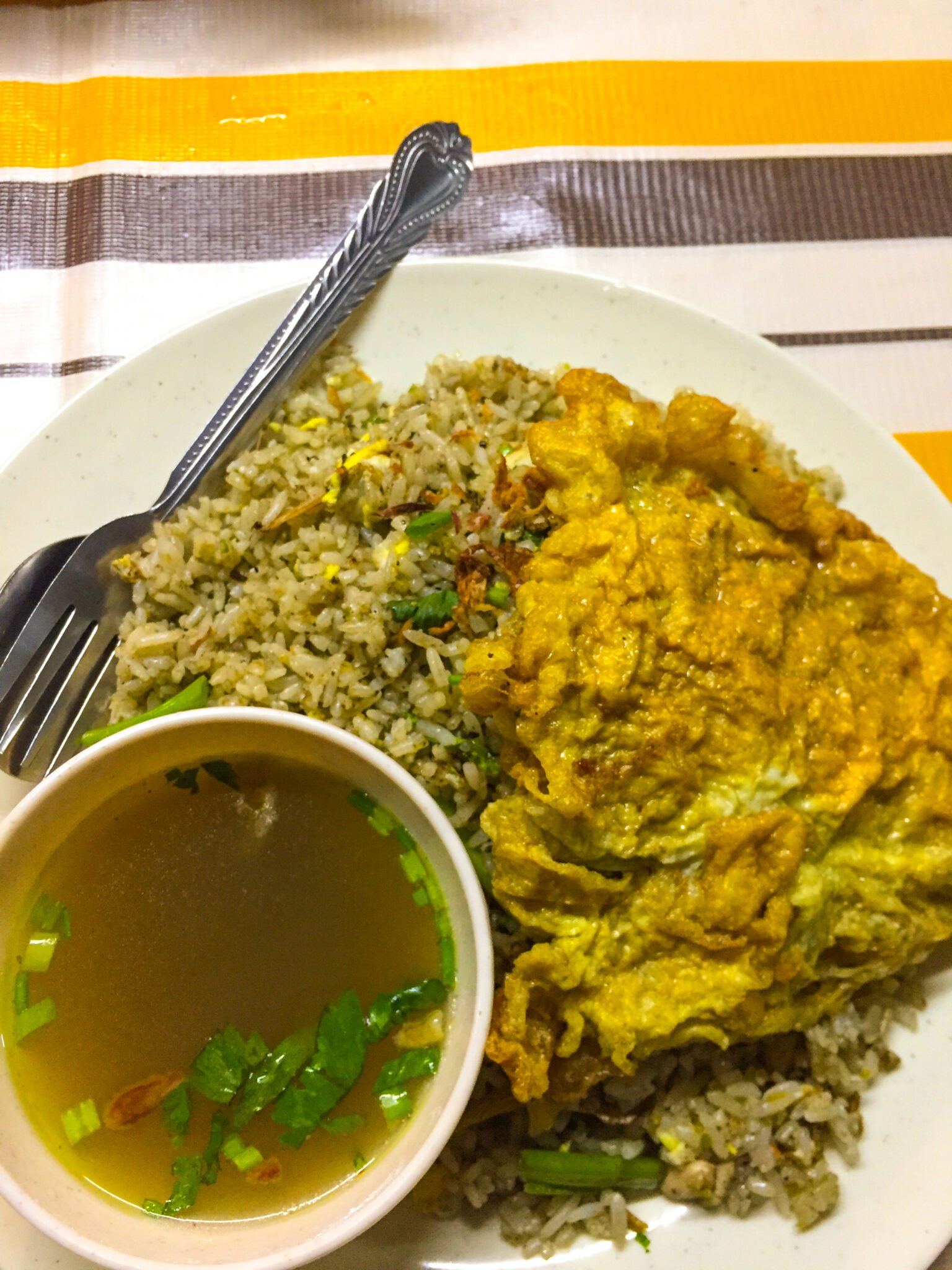 Sepinggan nasi goreng kampung dengan telur dadar dan semangkuk sup.