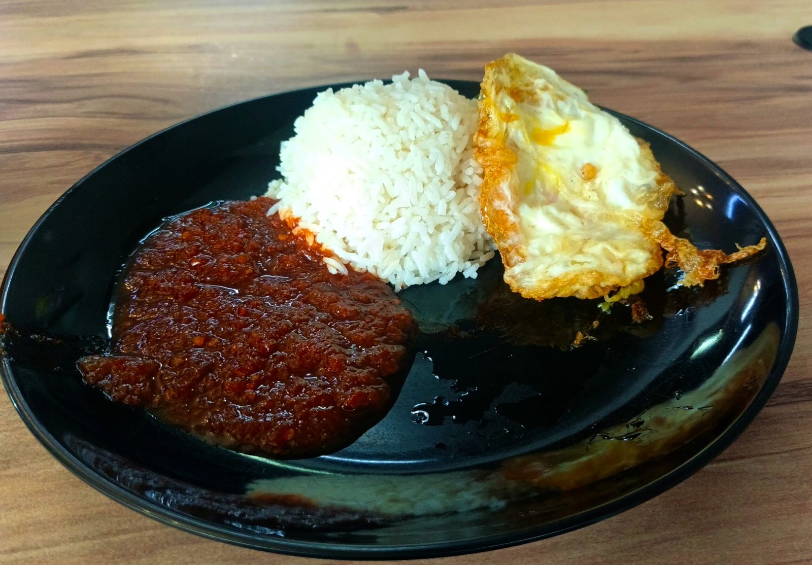 Nasi lemak di atas pinggan dengan sambal dan telur goreng.