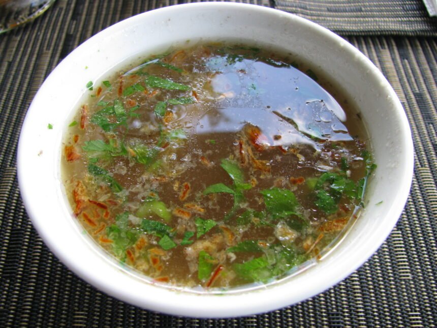 Semangkuk sup ayam jernih bertabur daun hijau dan bawang goreng.
