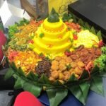 Celebratory Indonesian tumpeng with yellow rice and assorted side dishes