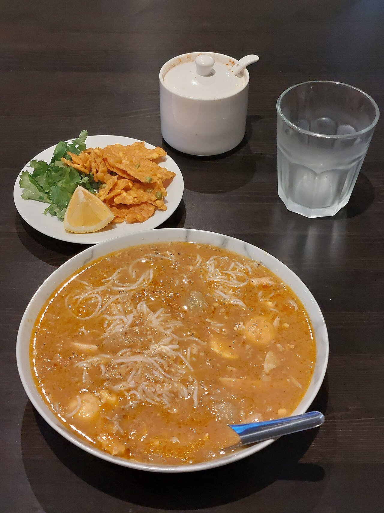 A bowl of mohinga with rice noodles, fritters, herbs and lime served at a Burmese restaurant