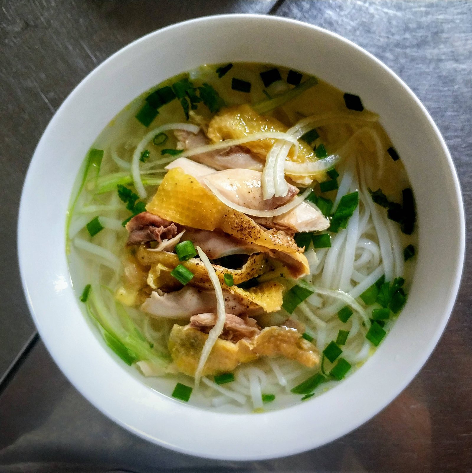 A separate bowl of Vietnamese chicken pho with rice noodles and sliced onion