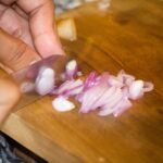Cook chopping shallots on a wooden cutting board