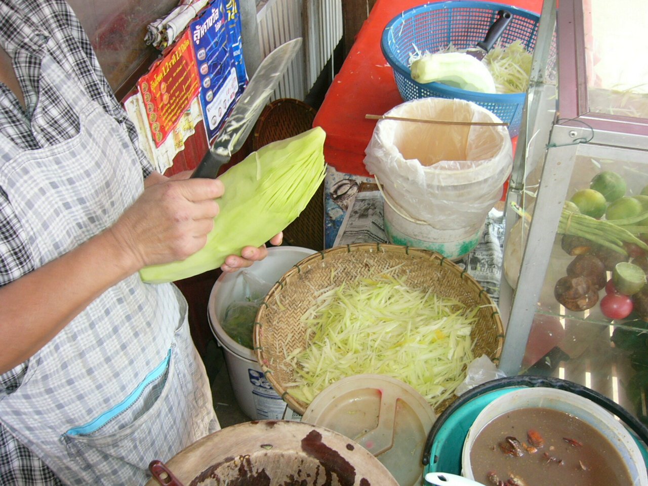 Street-food cook shredding green papaya for som tam in Si Songkhram, Thailand