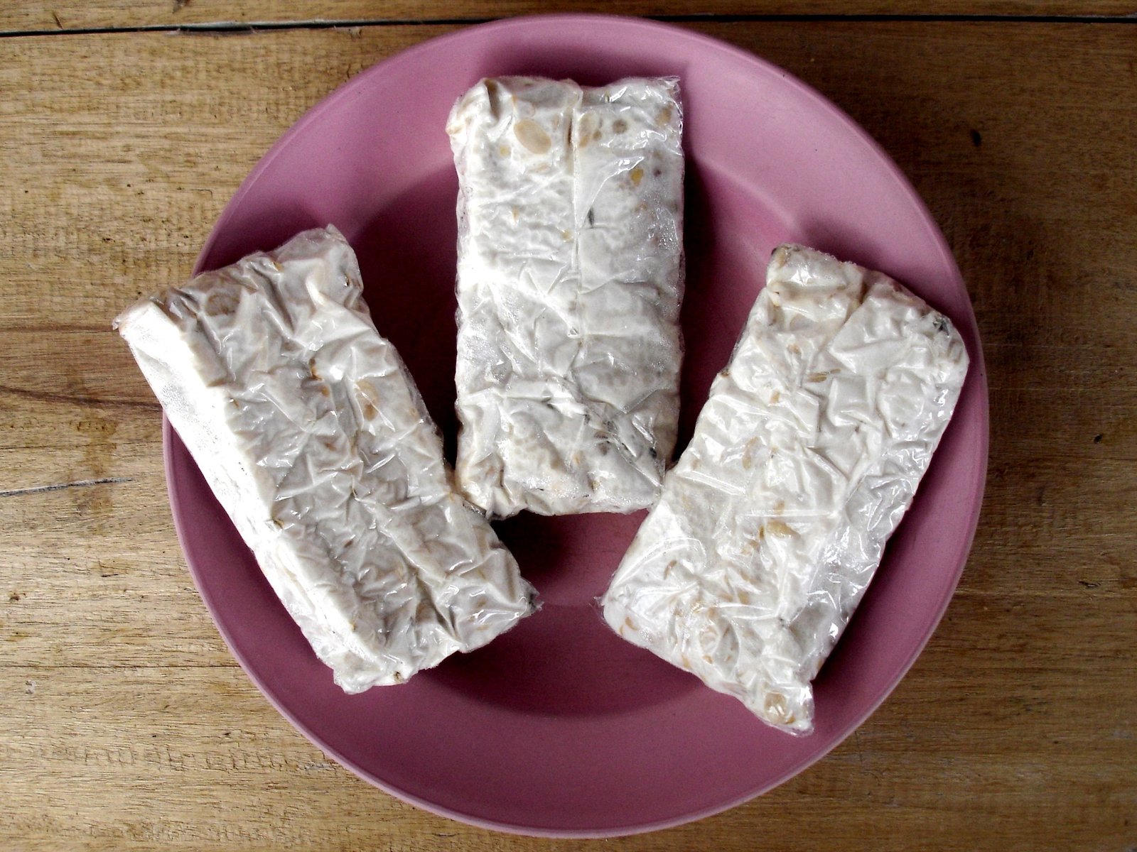 Three fresh blocks of tempe from an Indonesian market on a pink plate