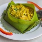 Cambodian fish amok served in a folded leaf cup on a white plate