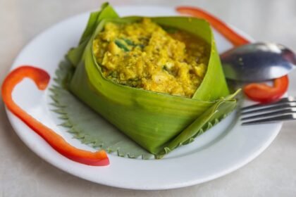 Cambodian fish amok served in a folded leaf cup on a white plate