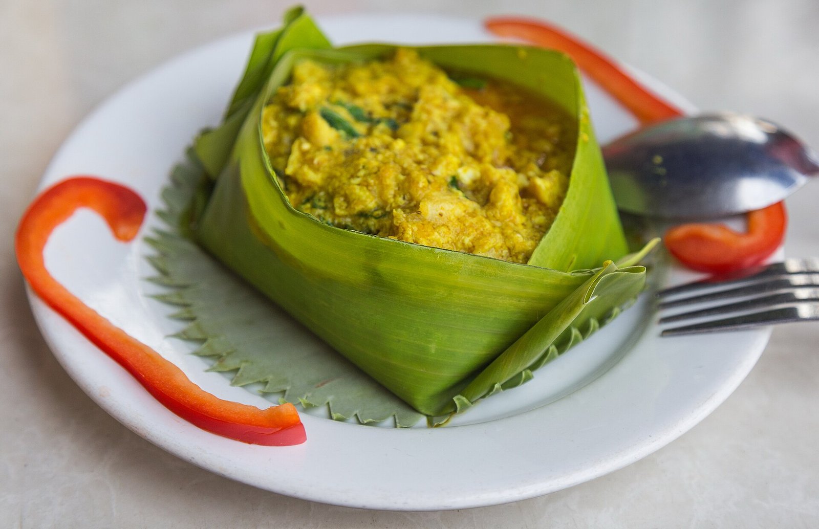 Cambodian fish amok served in a folded leaf cup on a white plate