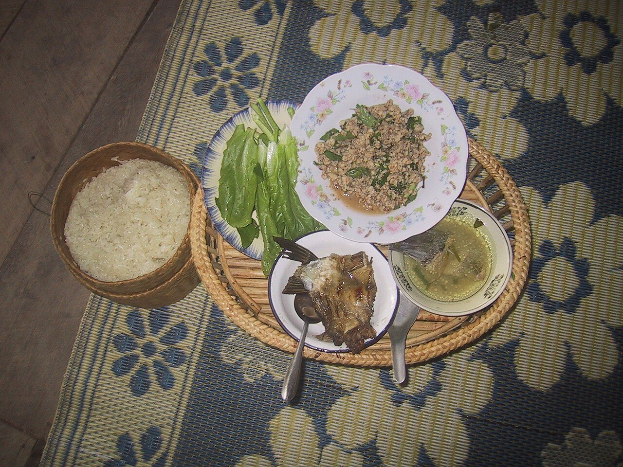 Shared Lao meal on a tray with fish larb, grilled fish, soup, salad and sticky rice